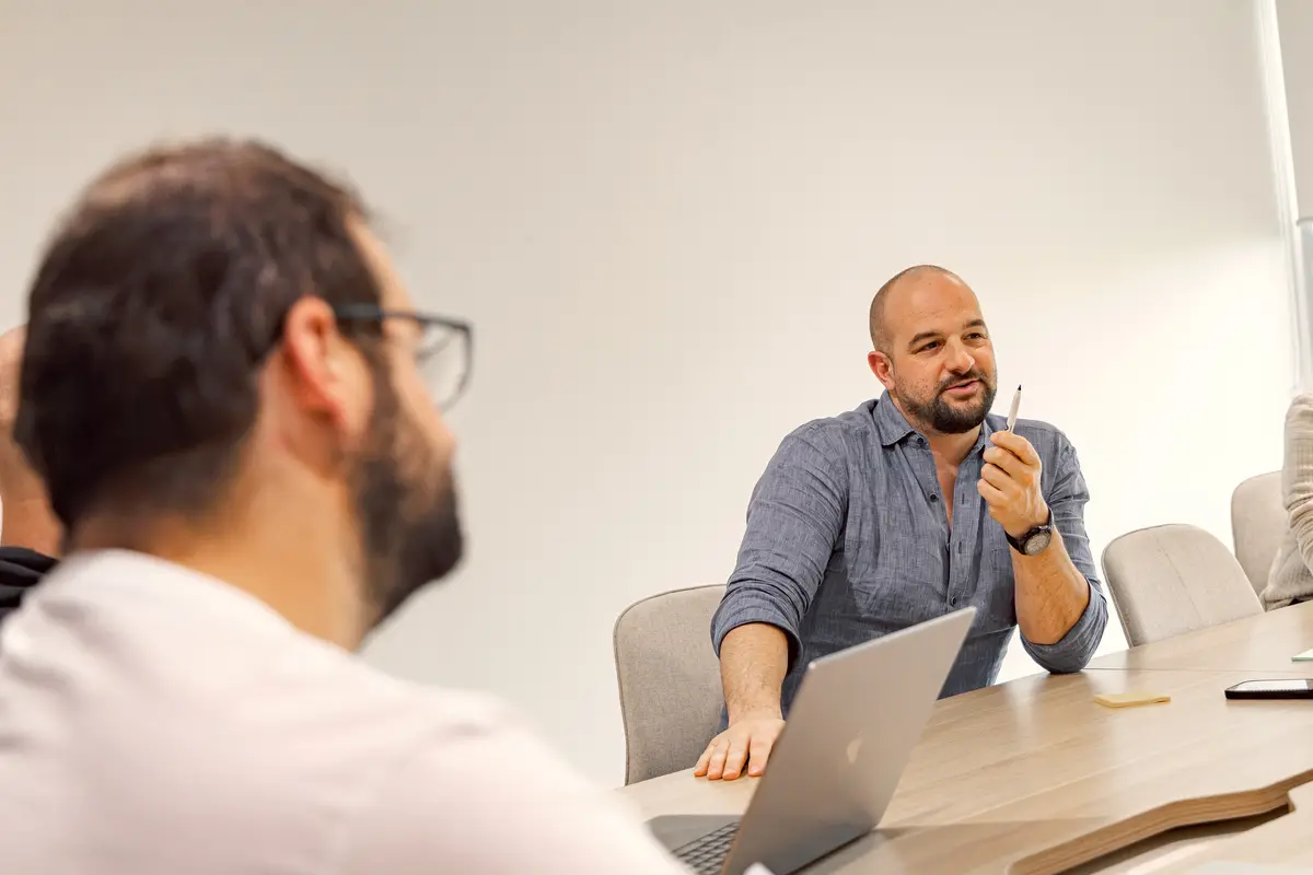 A man gesturing with a pen while talking in a meeting room