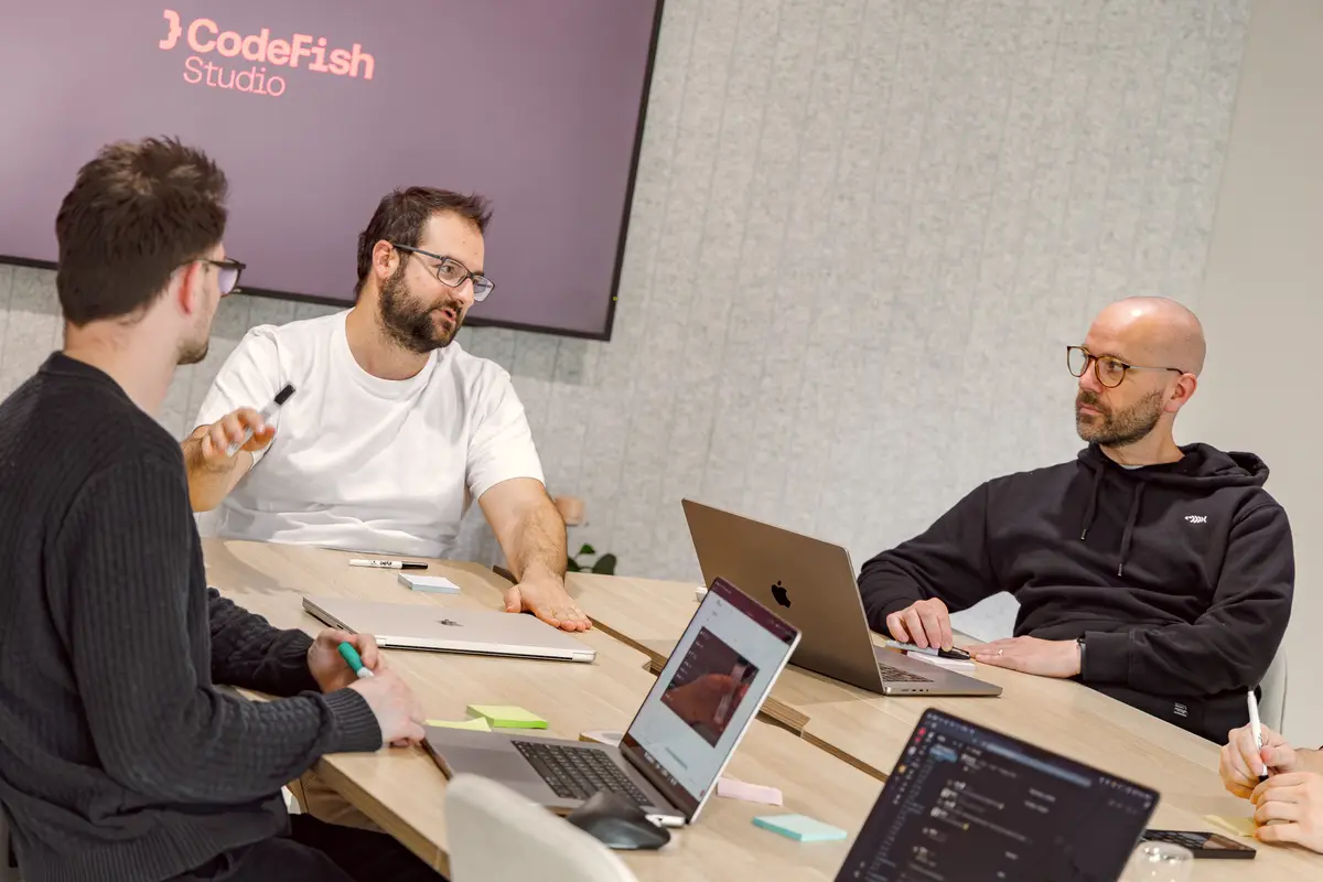 Four CodeFish team members talking around a meeting table with laptops