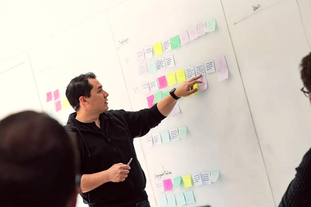 A facilitator pointing to sticky notes on a whiteboard during a workshop