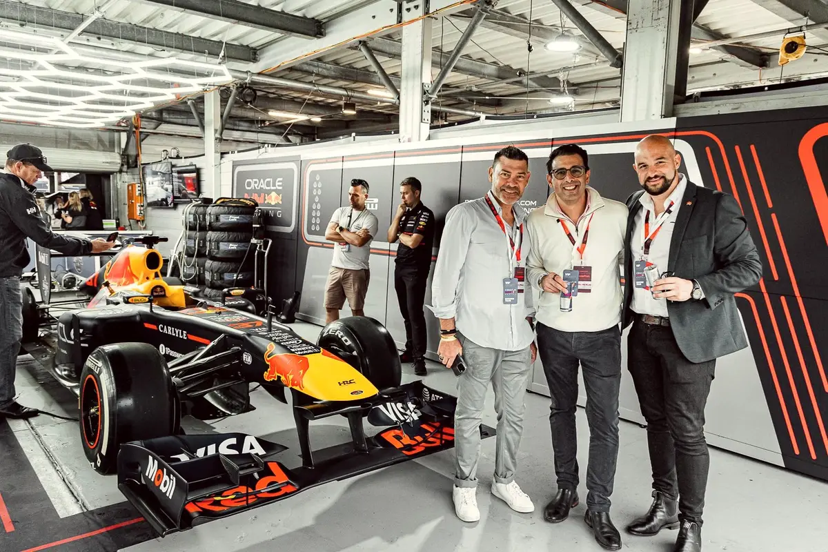 Three guests with VIP passes beside a Red Bull Racing Formula 1 car in the garage