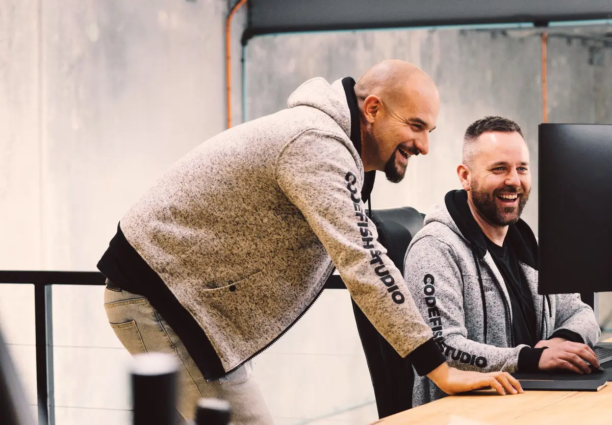 Two CodeFish Studio team members laughing together at a computer