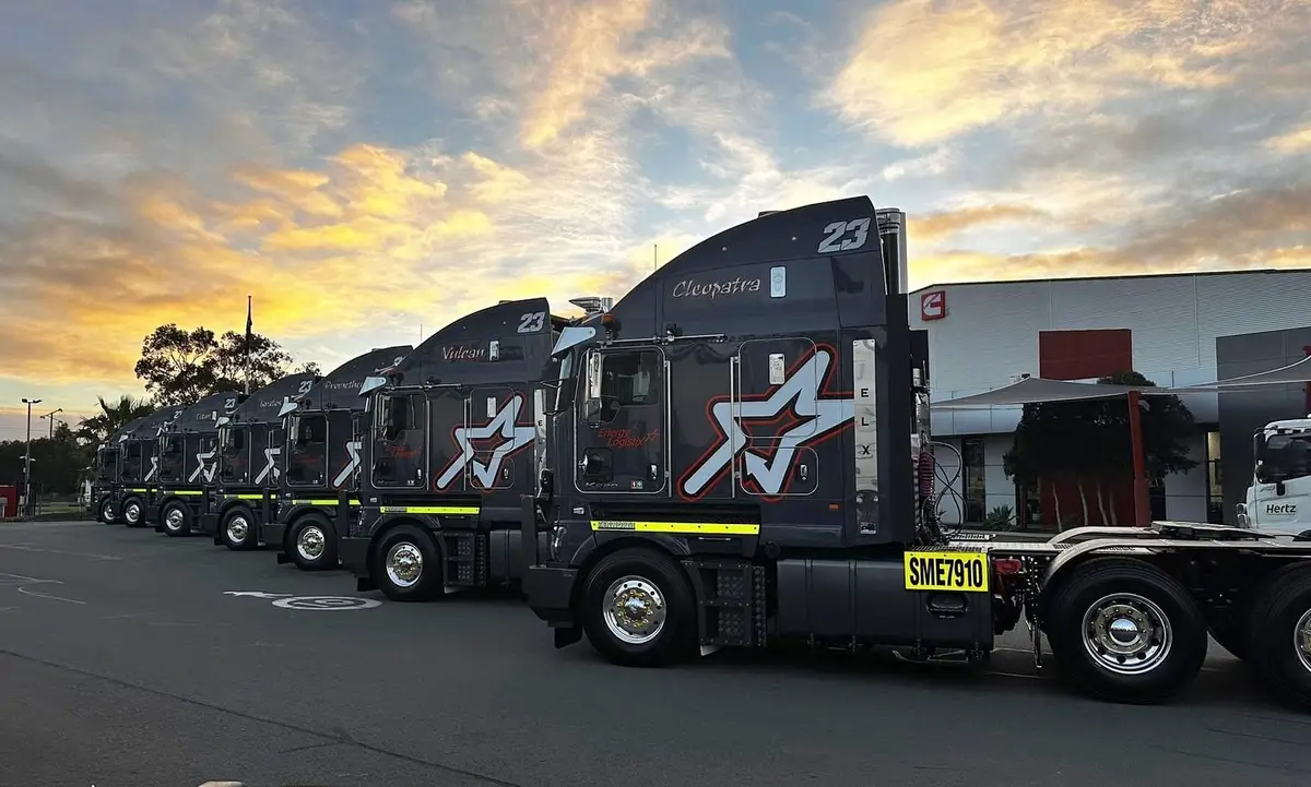 Row of dark Energy Logistix prime mover trucks parked at sunset
