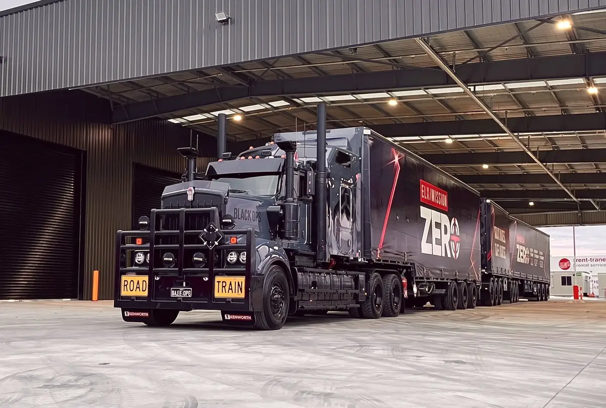 Black Kenworth road train with Mission Zero trailers parked under a depot canopy
