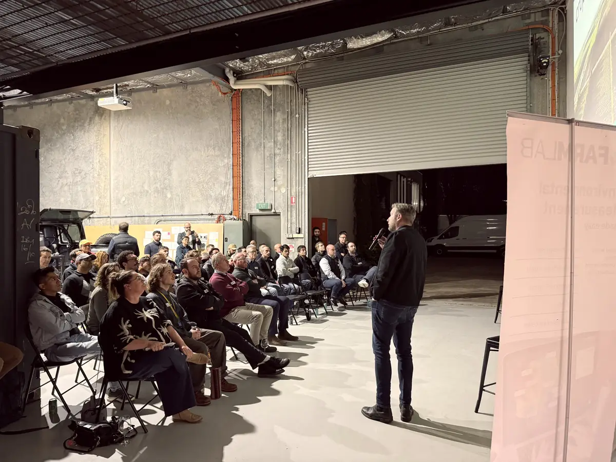 Speaker with a microphone presenting to a seated audience in a warehouse event space