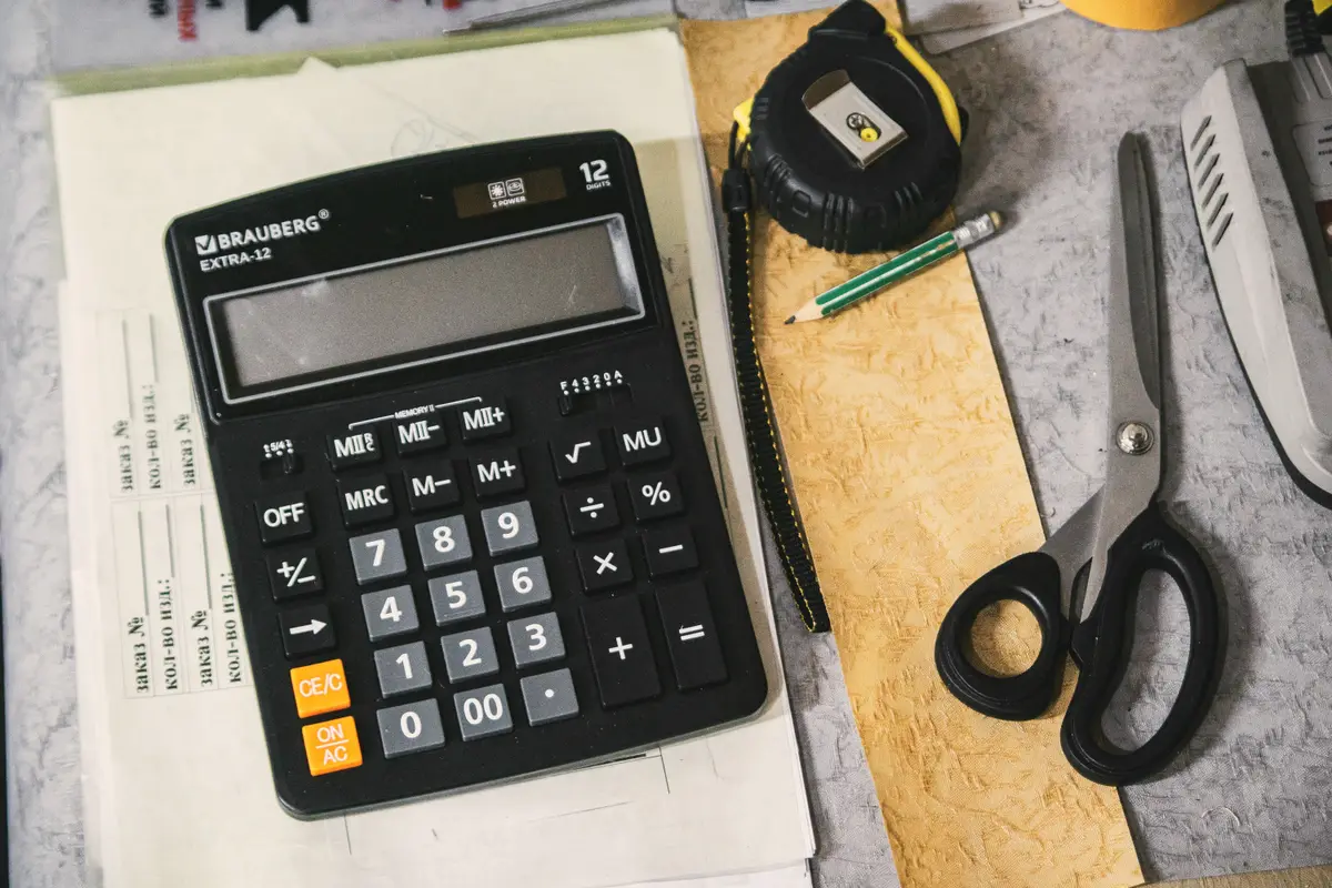 Calculator, tape measure, pencil and scissors on a desk with paperwork