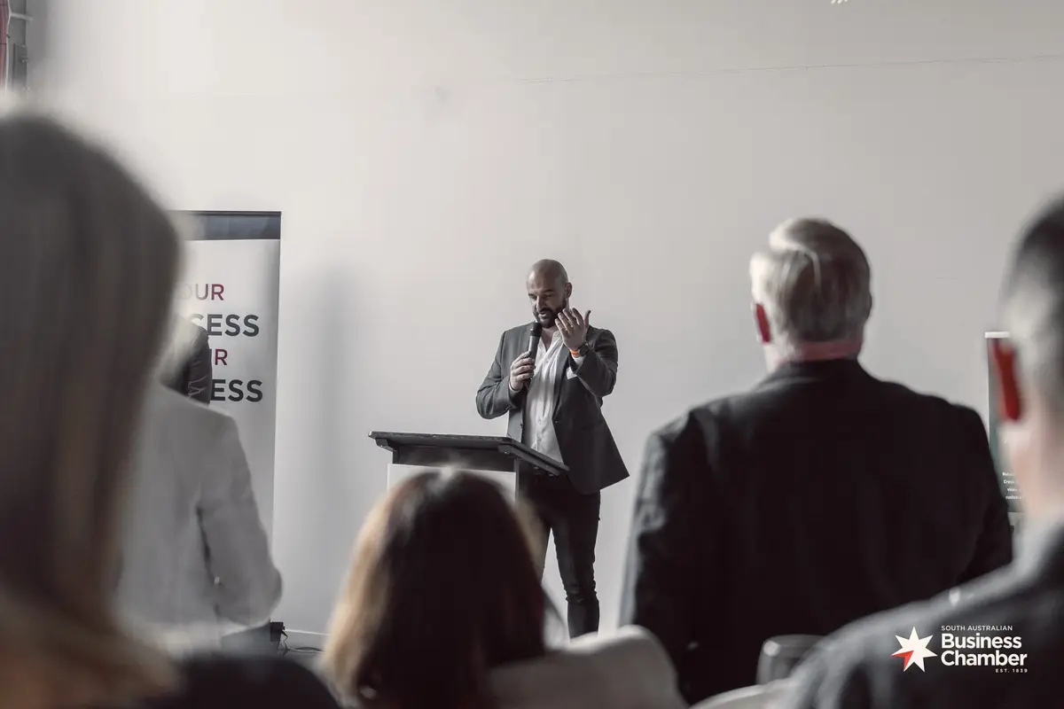 Speaker with a microphone at a lectern addressing an SA Business Chamber audience