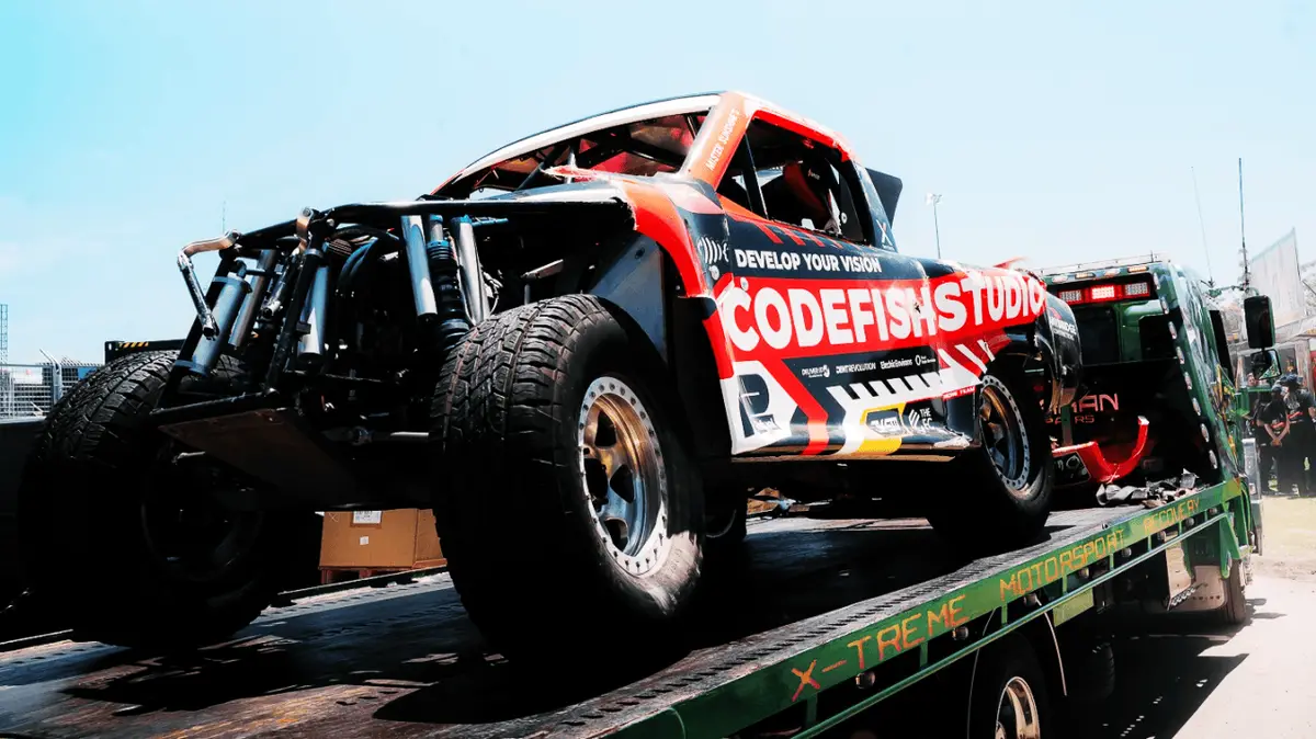 Damaged CodeFish Studio branded off-road race truck on an X-Treme Motorsport tow truck
