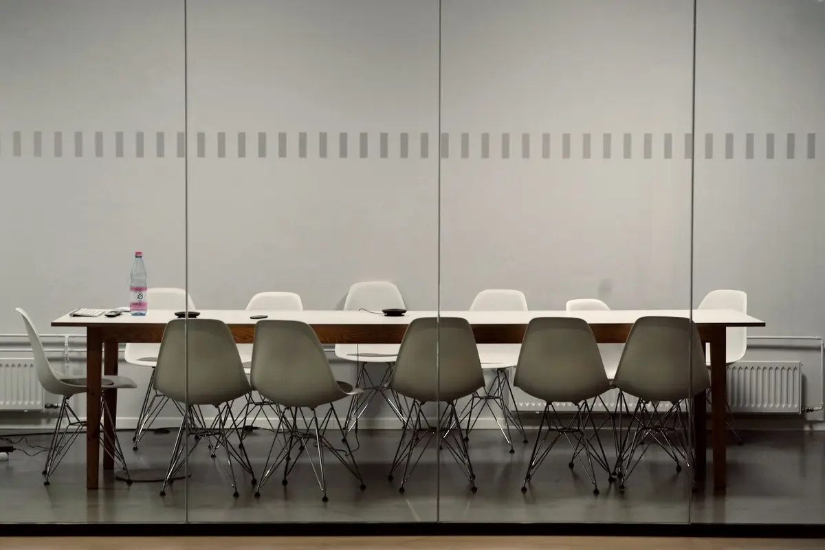 An empty boardroom with a long table, seen through a glass wall