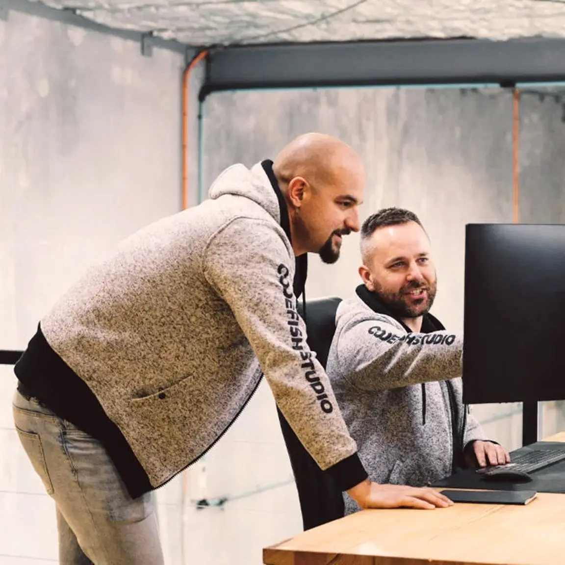 Two CodeFish team members in branded hoodies reviewing work on a monitor
