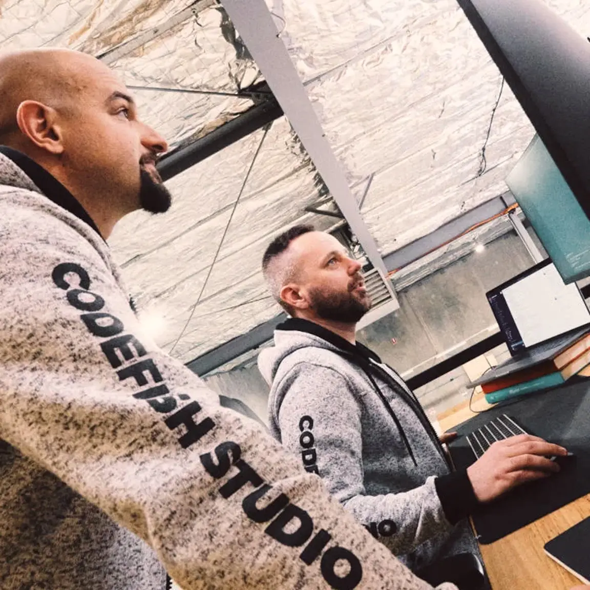 Two CodeFish team members in branded hoodies looking at a monitor