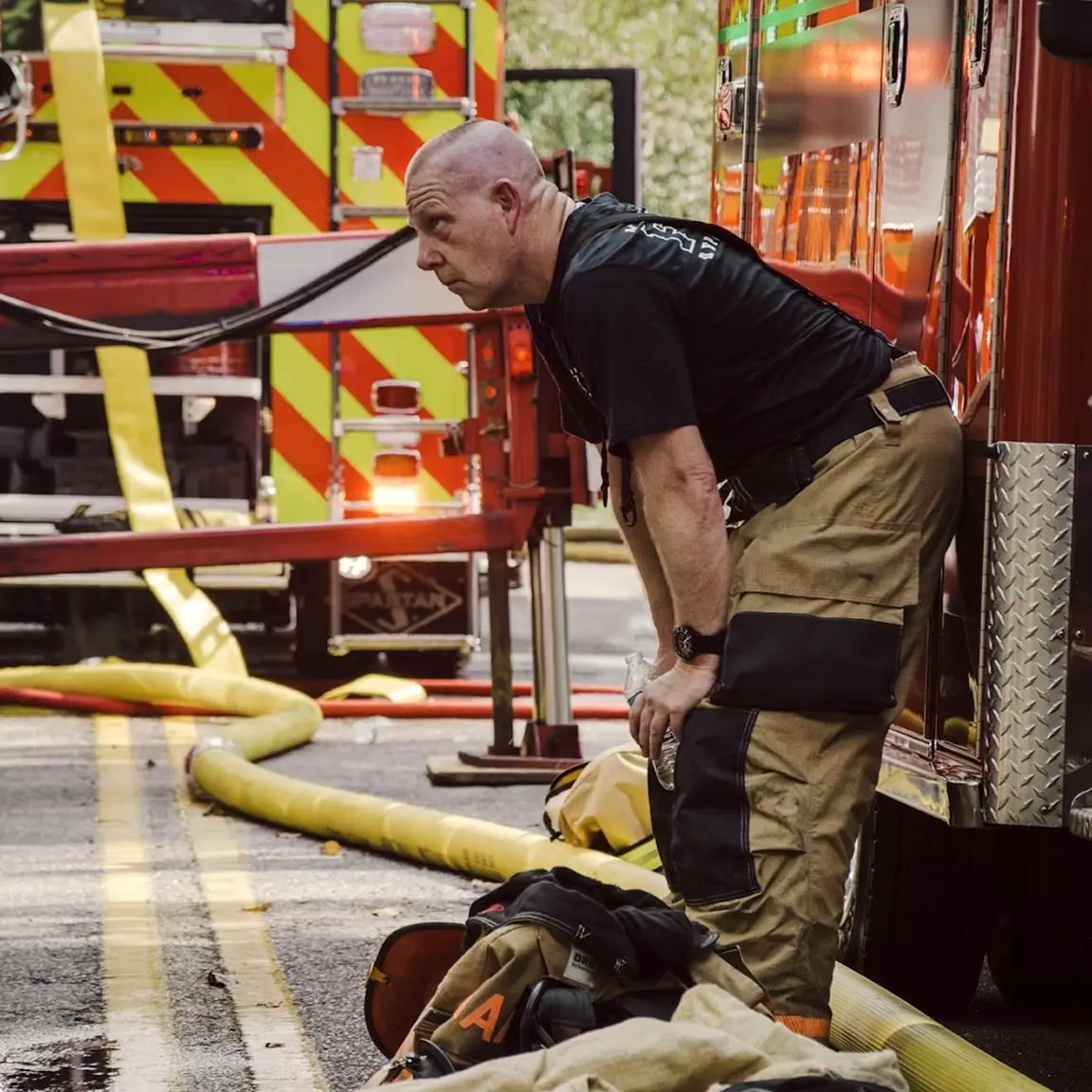 Firefighter resting beside a fire truck with hoses on the road