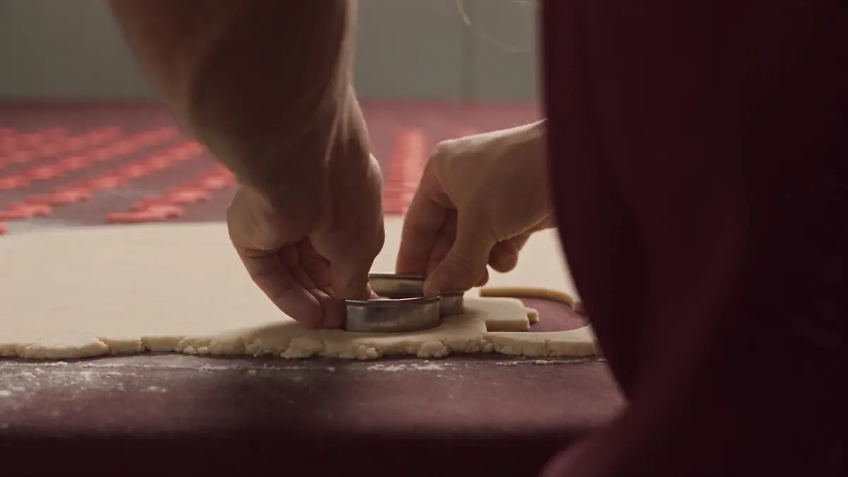 Hands pressing a metal cookie cutter into rolled dough