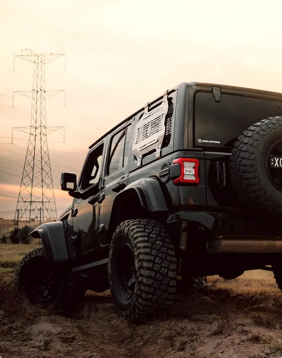 Lifted four-wheel drive with a slotted window storage panel parked in a paddock at sunset
