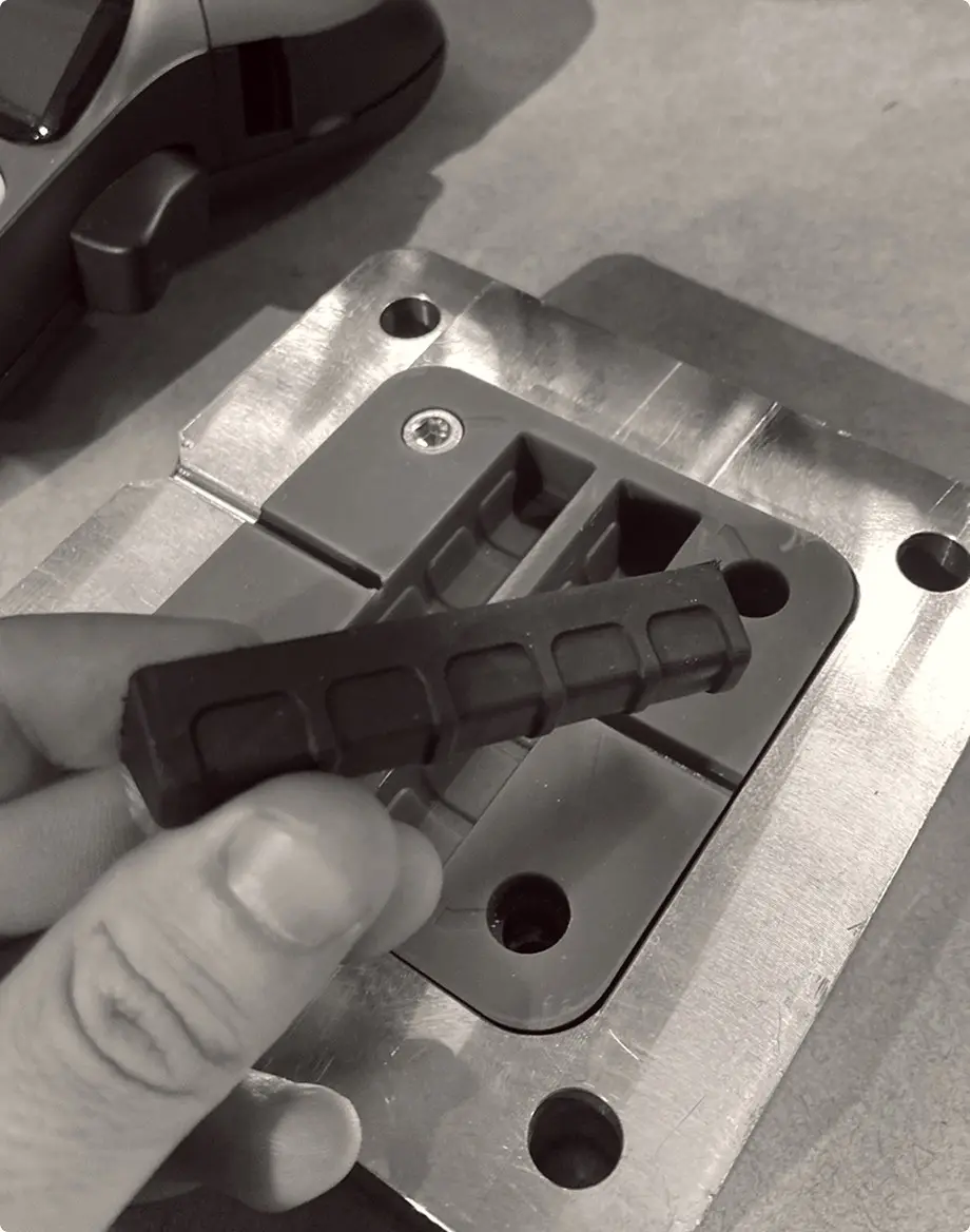 A hand holding a moulded rubber part beside its aluminium tooling block