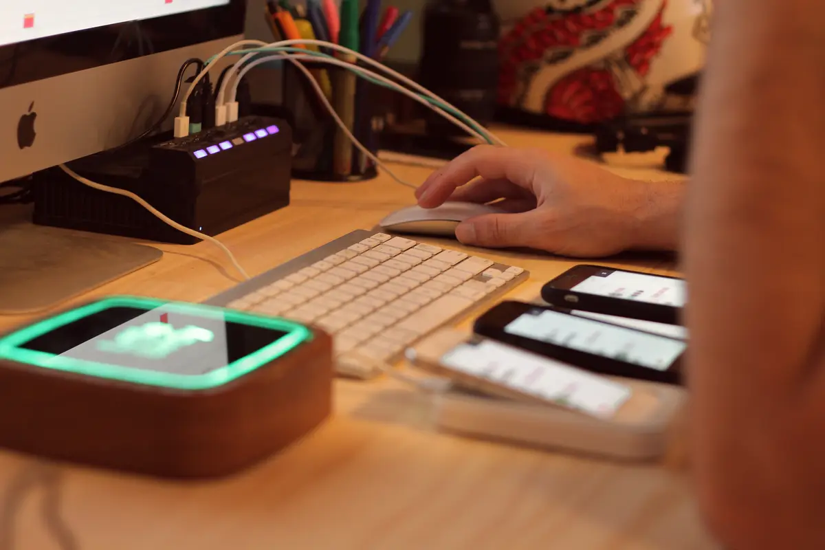Hand on a mouse at a desk with a keyboard, USB hub and several phones