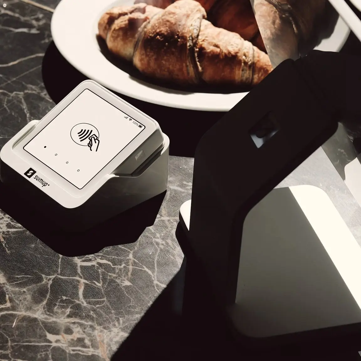 SumUp card payment terminal on a marble counter beside a plate of croissants