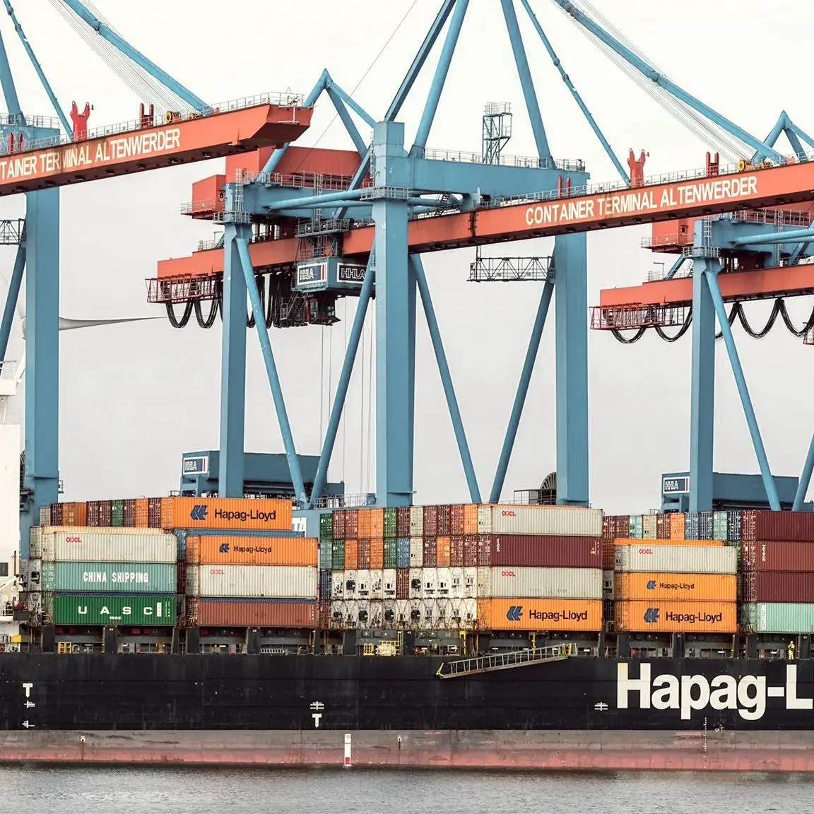 Container ship loaded with Hapag-Lloyd containers beneath port cranes