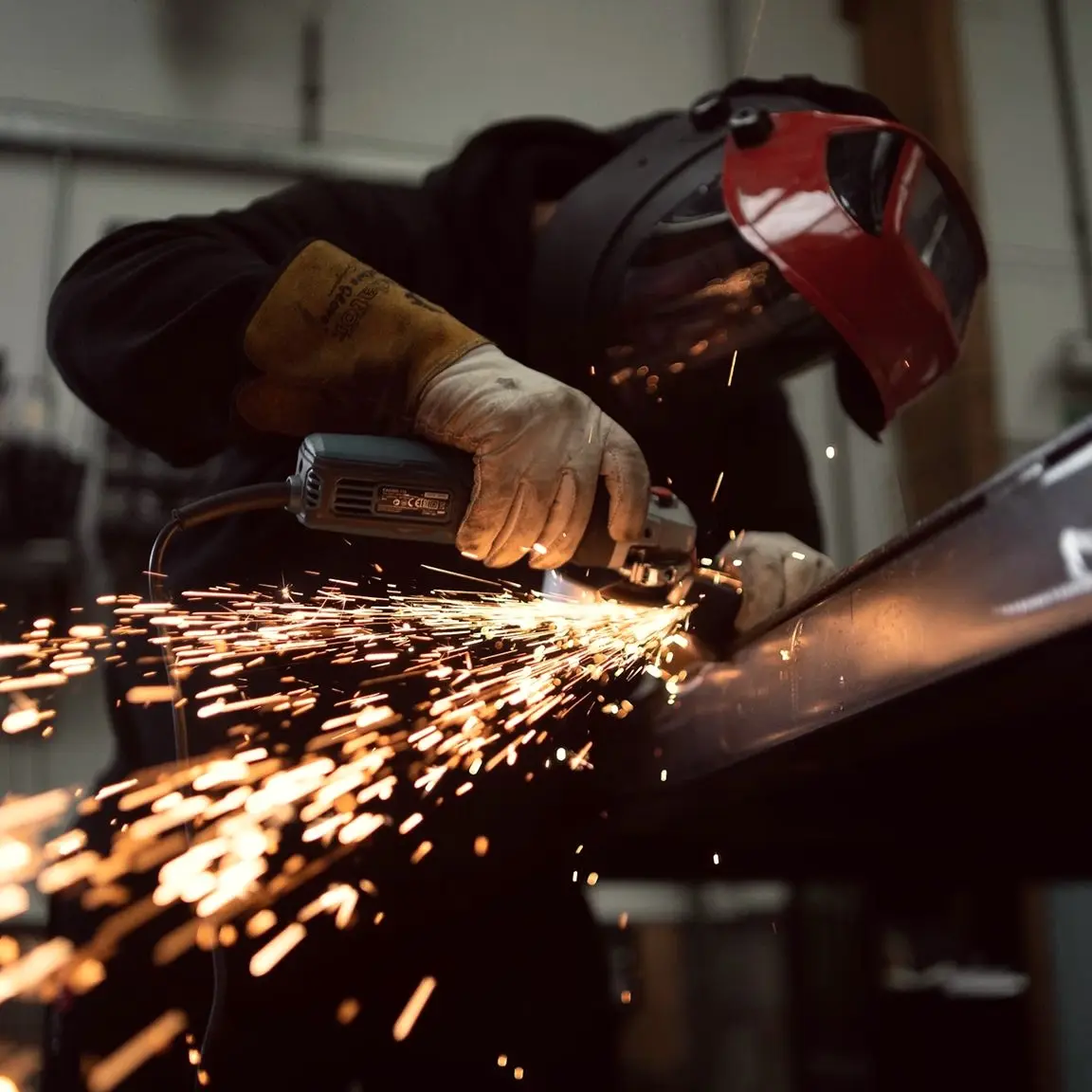 Welder in a red helmet grinding steel, sending sparks across the workshop