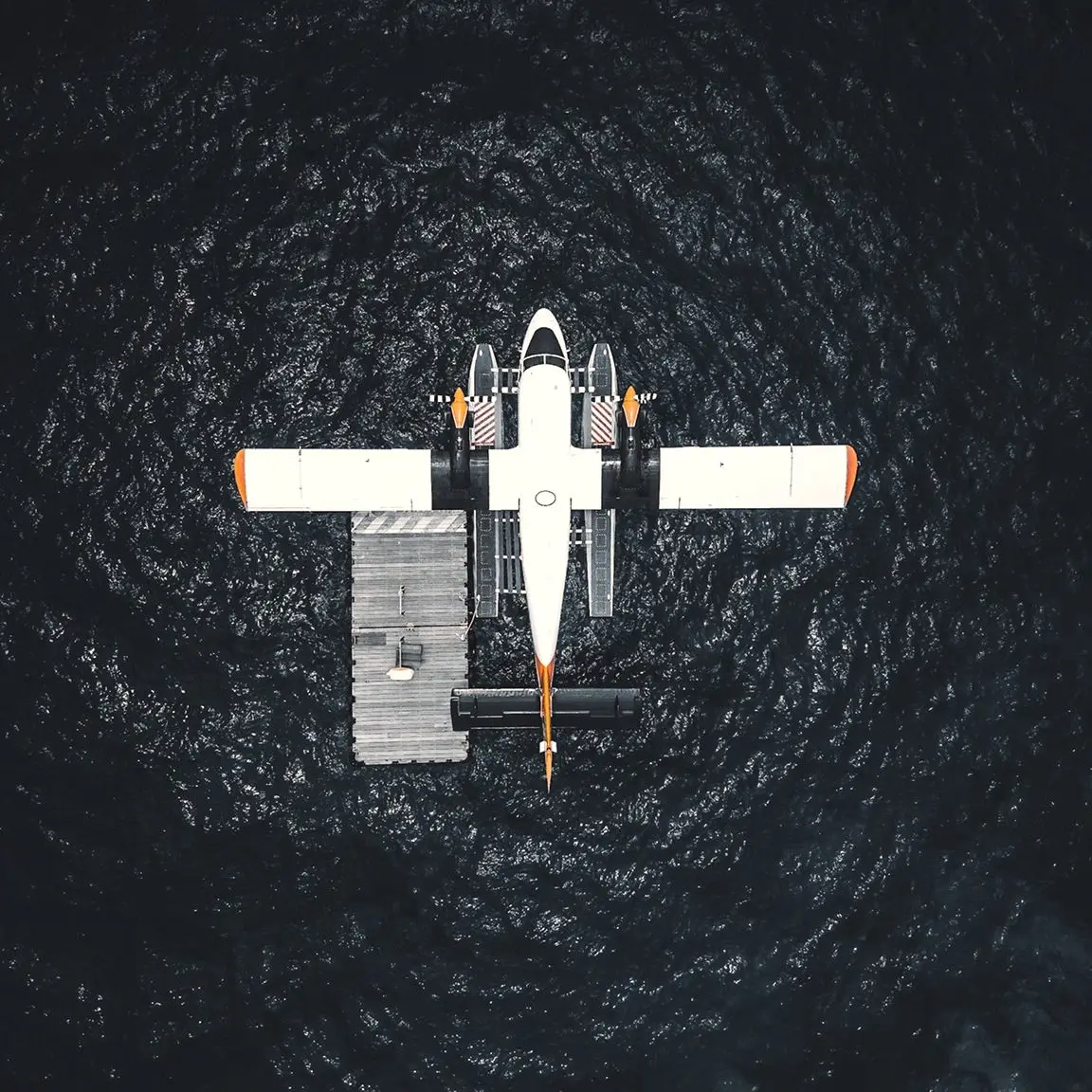 Aerial view of a white seaplane moored beside a floating dock on dark water