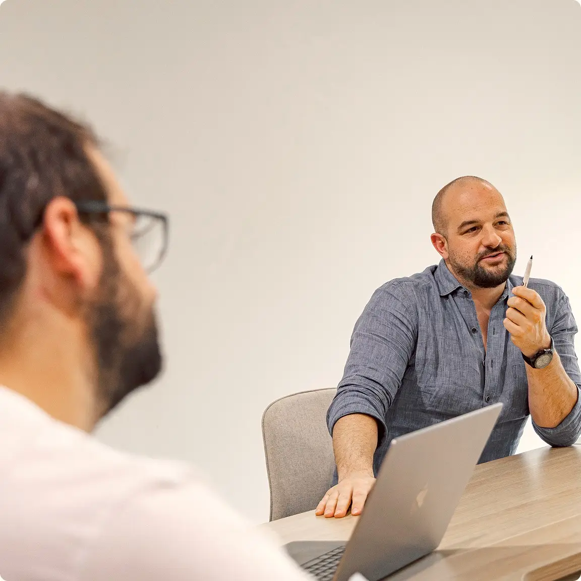 Two people in a meeting, one gesturing with a pen across a laptop