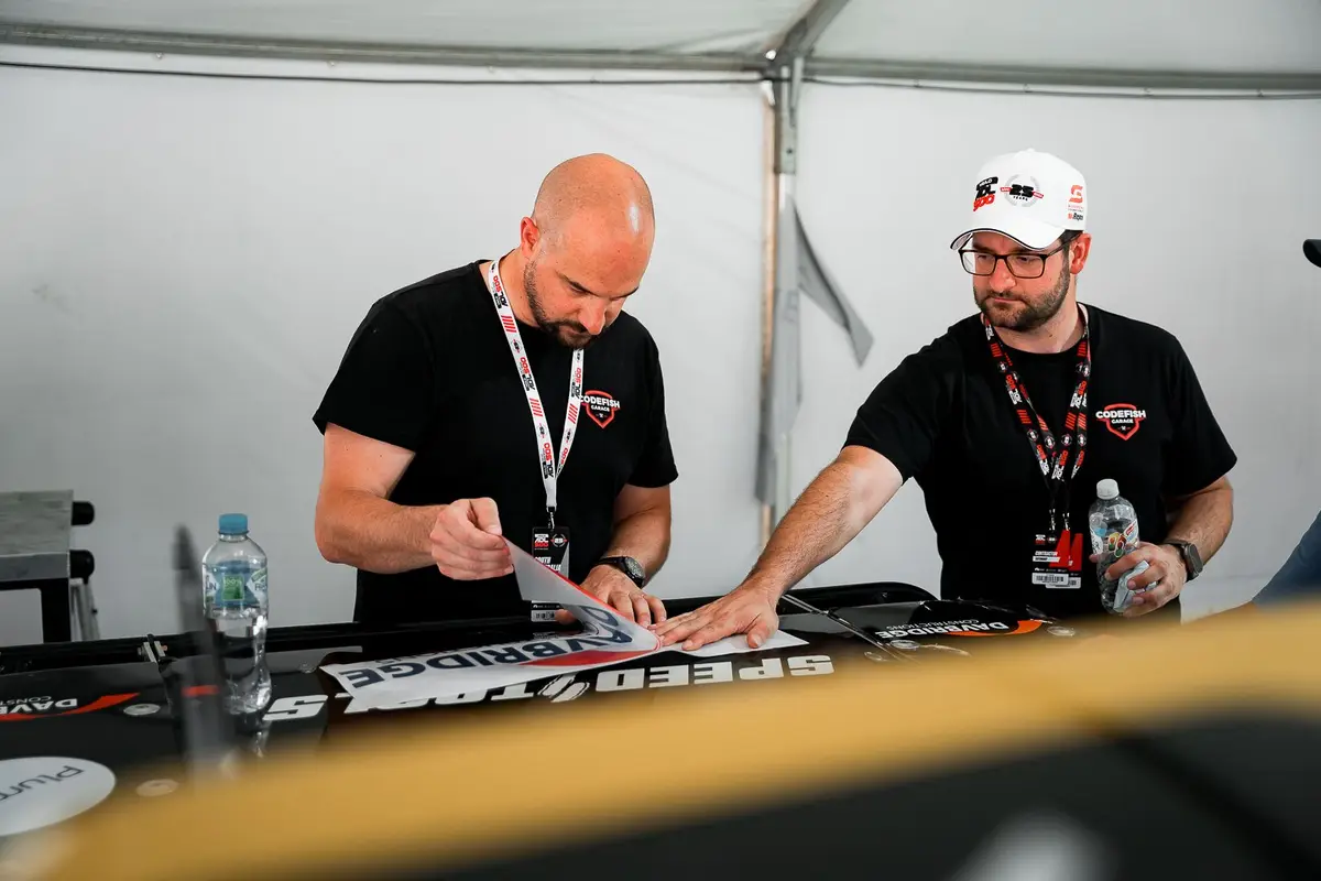 Two CodeFish team members applying sponsor decals to a race truck panel