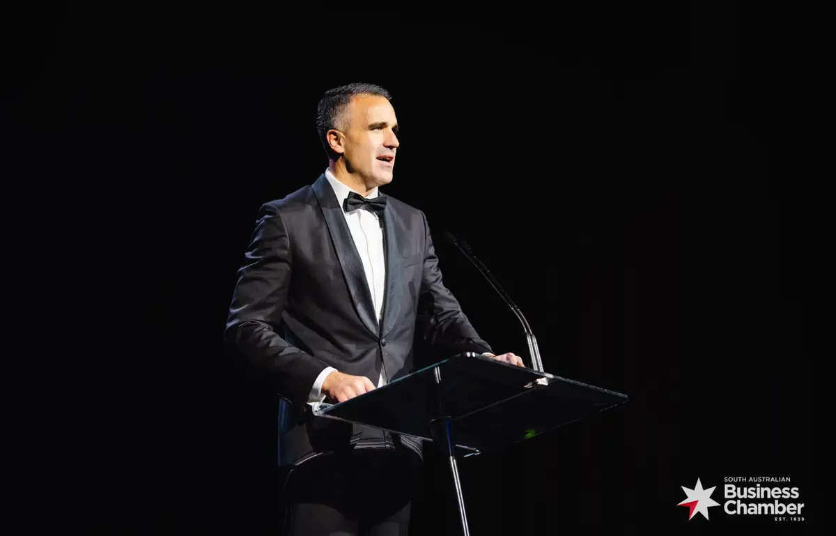 Man in a tuxedo speaking at a glass lectern, South Australian Business Chamber logo