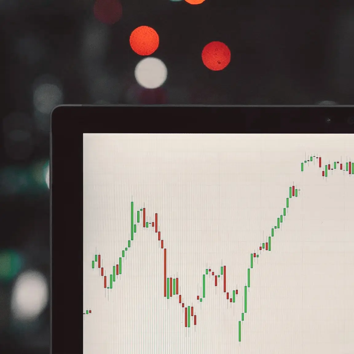 Laptop screen showing a candlestick stock chart against blurred city lights