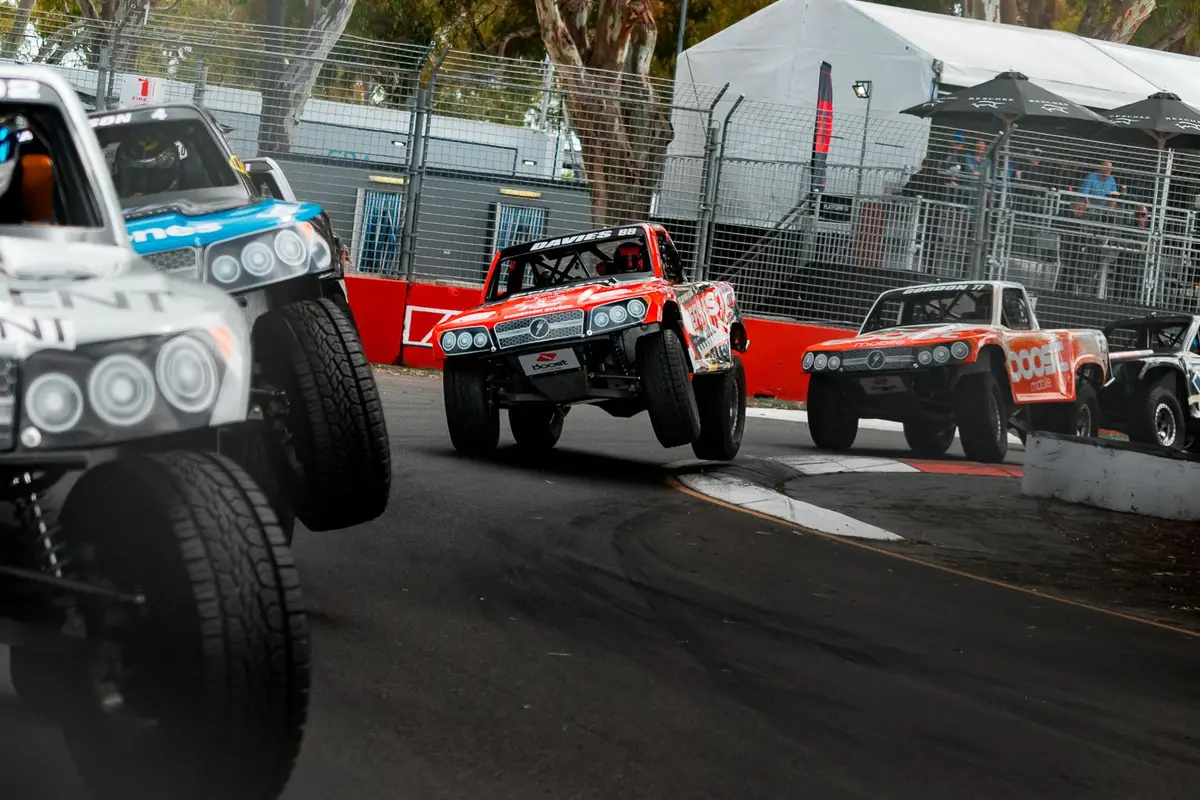 Stadium trucks racing through a corner, number 88 lifting a wheel over the kerb