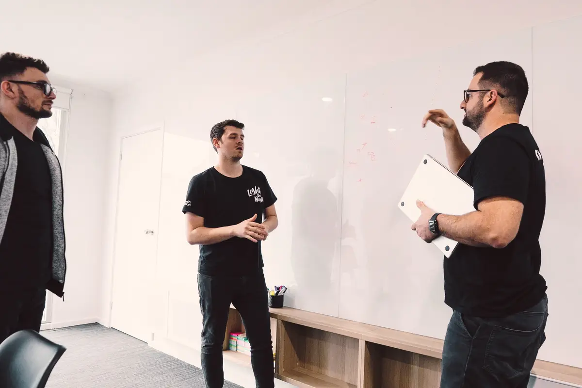 Three CodeFish team members talking in front of a whiteboard wall