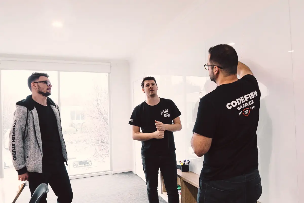 Three CodeFish team members discussing ideas beside a whiteboard in a bright office