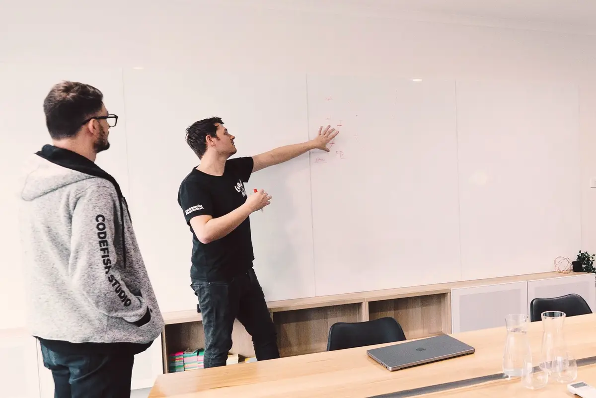 Two CodeFish team members scoping ideas on a whiteboard wall in a meeting room