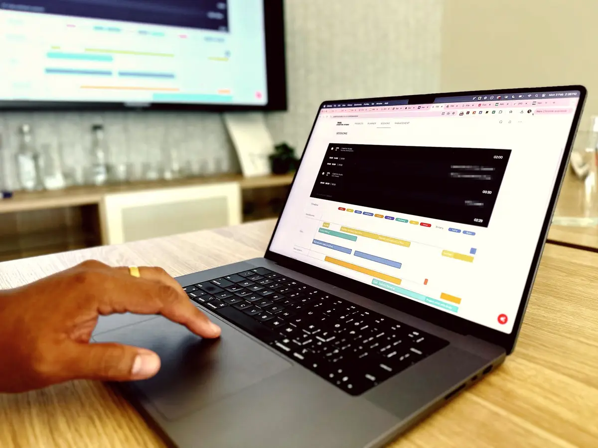 Hand on a laptop trackpad showing a scheduling dashboard with coloured timeline bars